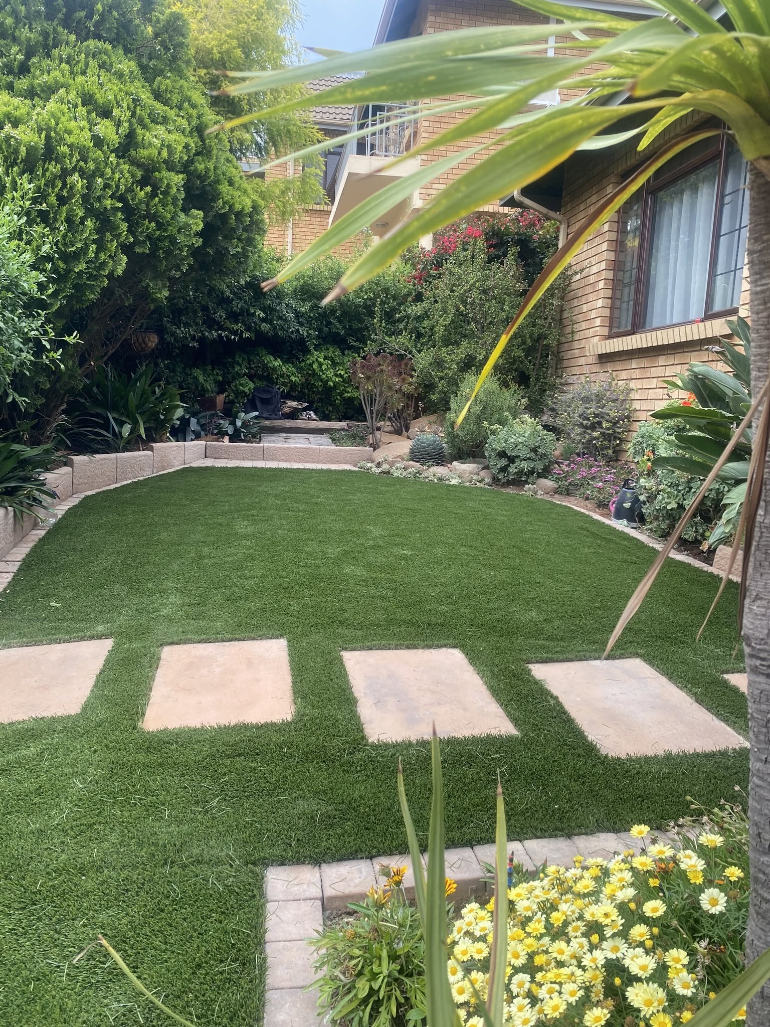 Circular artificial lawn edged with paving and a planted garden bed.
