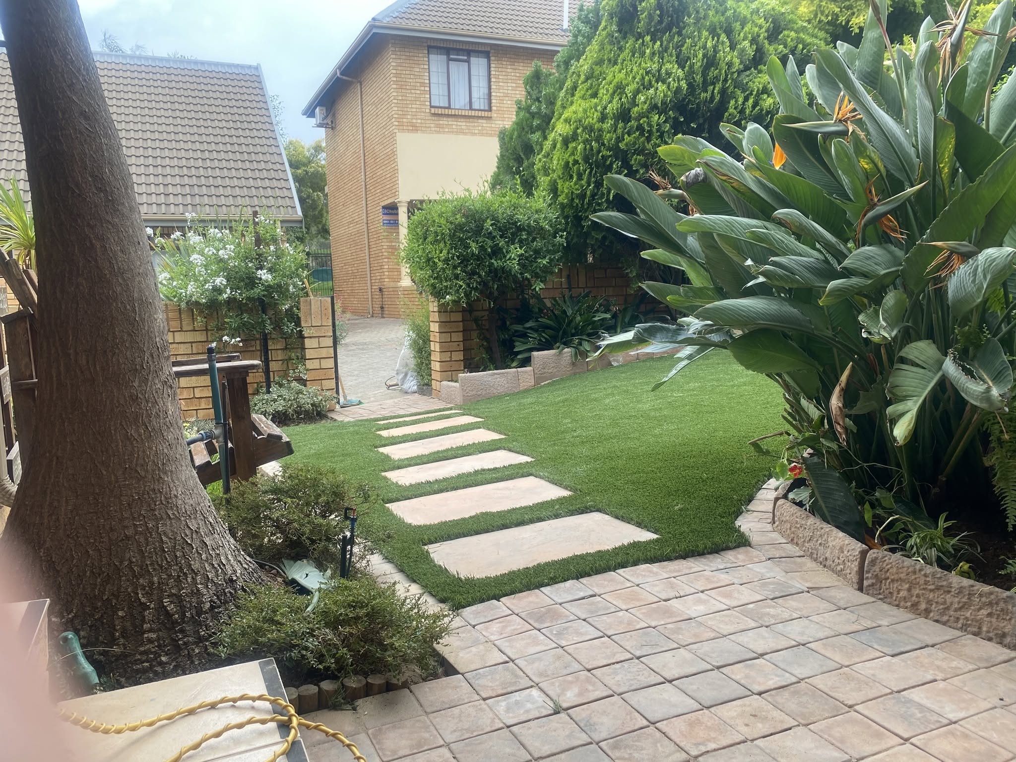 Stepping-stone path across an artificial lawn leading to a paved patio.