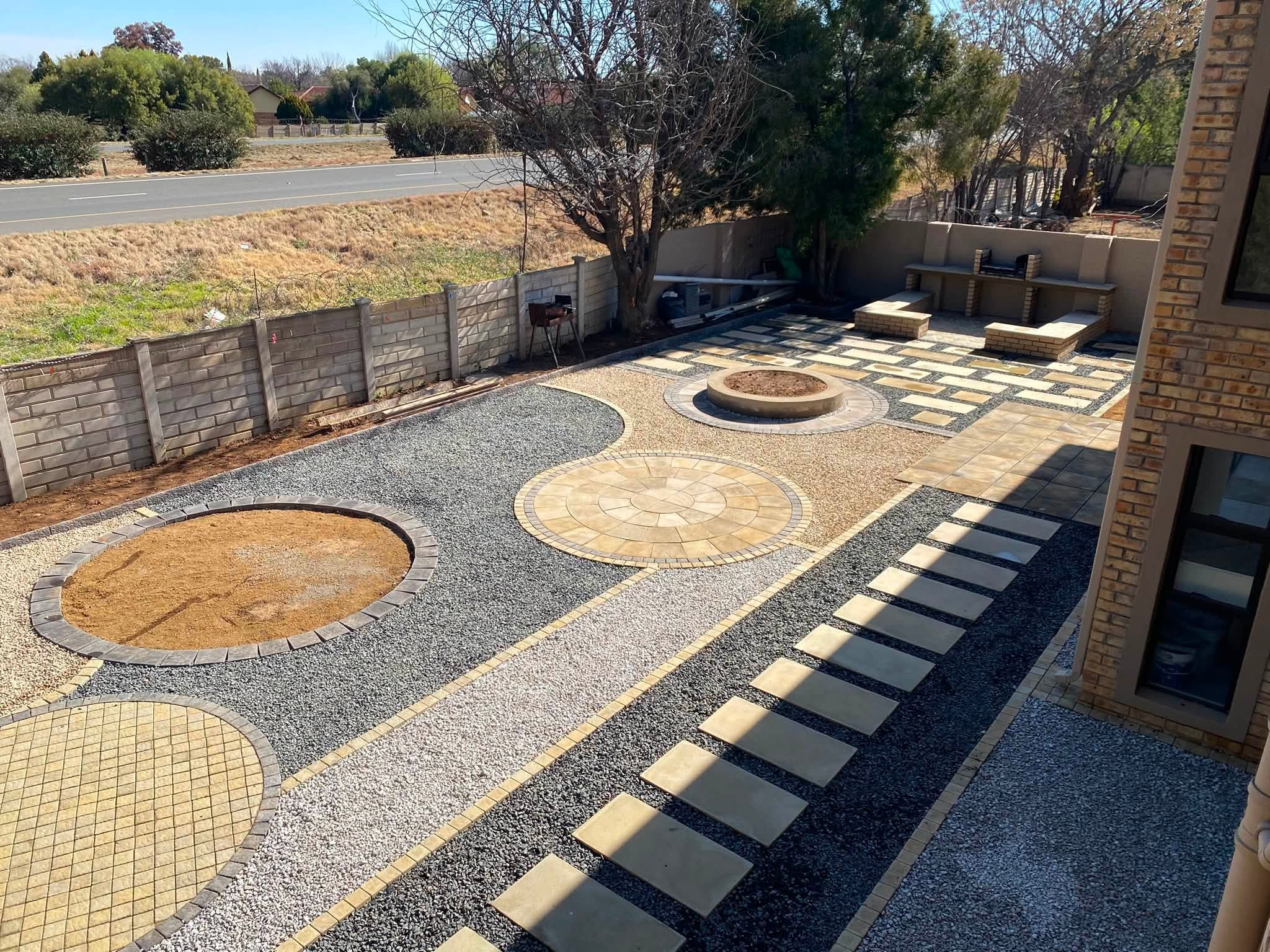 Paved courtyard with circular paving medallions, gravel landscaping and a fire-pit area, viewed from the house.