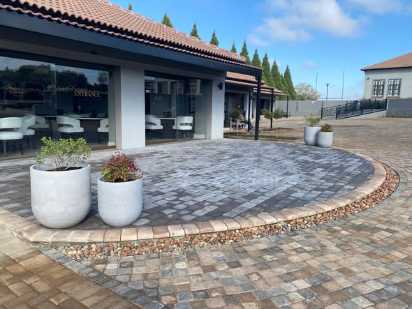 Circular entrance paving outside a Bloemfontein guesthouse, with potted plants and a tiled-roof building.